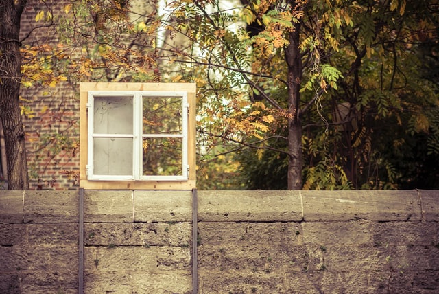 une fenêtre dans un chassis en bois est posée sur un muret délimitant un jardin