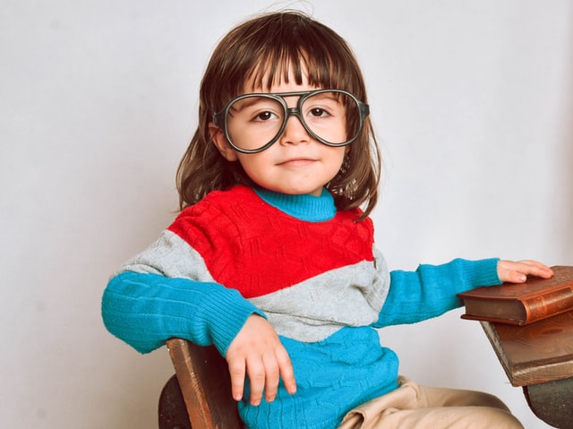 petite fille avec un pull à rayures et de grandes lunettes assise à une table d'école